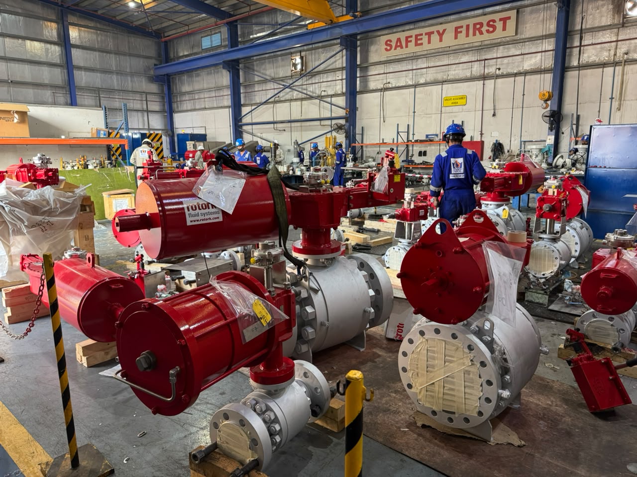 Actuated ball valves on pallets in a valve assembly bay, with technicians working in the background